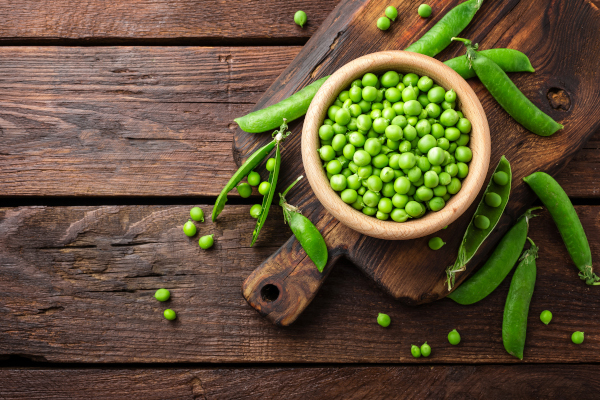 Photo of peas in bowl with pods laying on the table. 